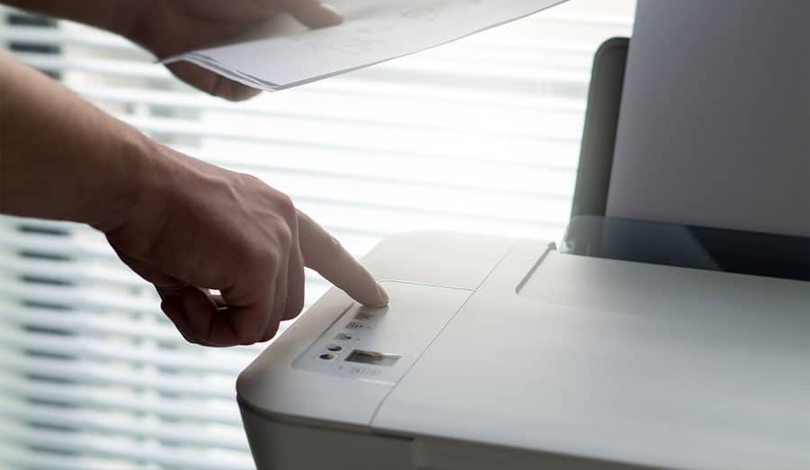 A person holding a stack of papers while pushing a button on a printer