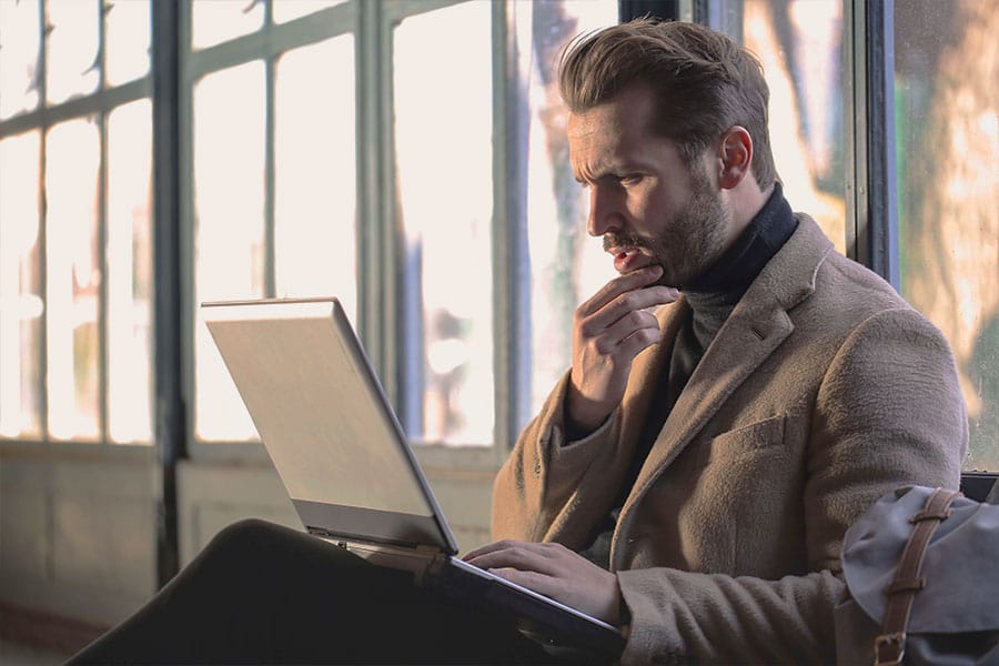 A man looking at his laptop screen while stroking his beard