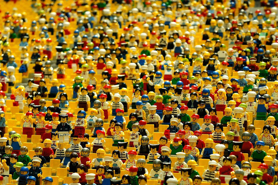 Hundreds of different lego figurines sitting in rows of stadium chairs.