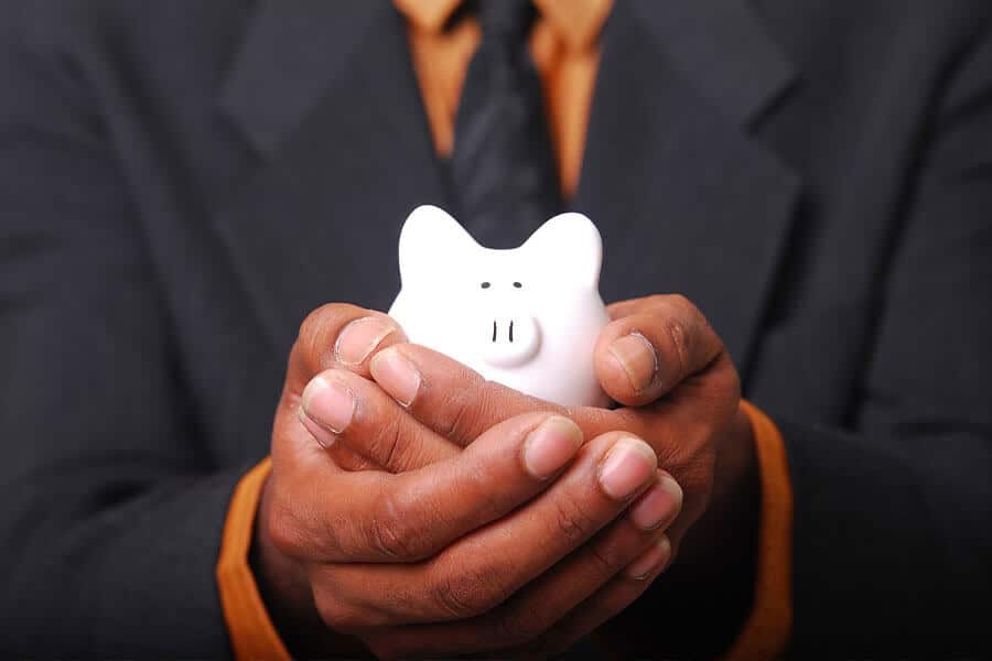 A man in a suit holding a small, white piggy bank