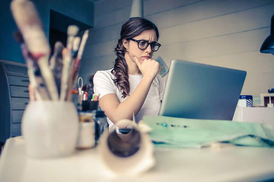 an image of a woman sitting at a craft desk looking at her laptop screen.