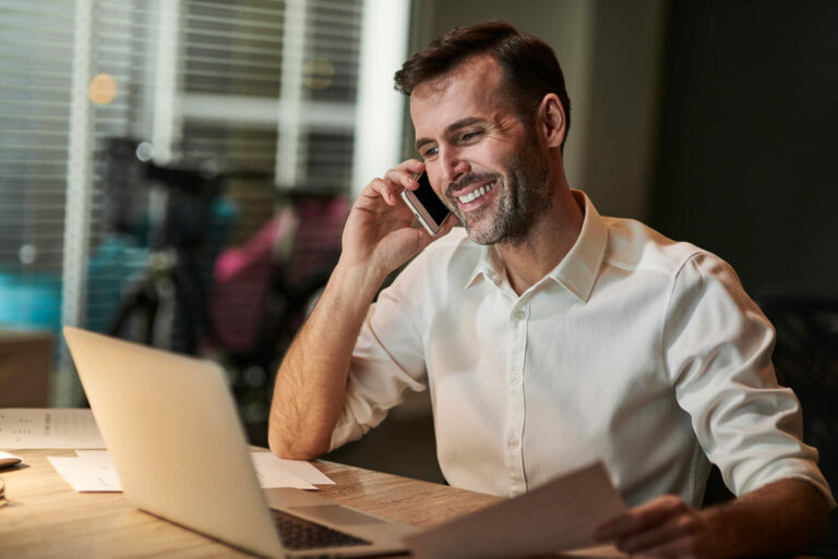 smiling businessman talking on the phone with an open laptop in front of him