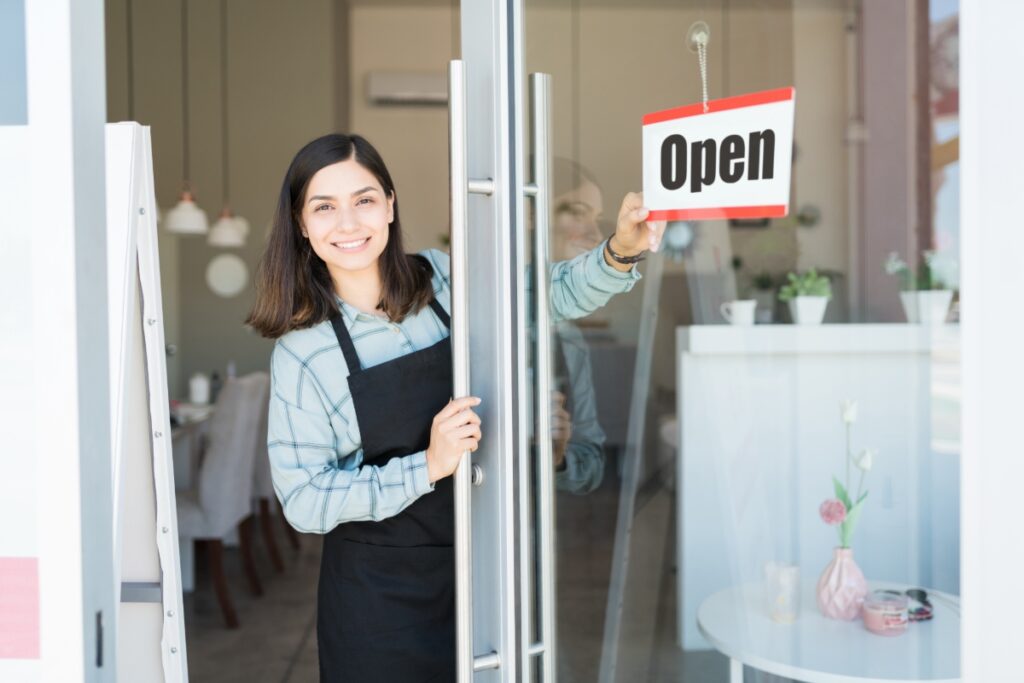 woman putting up open sign in front of business