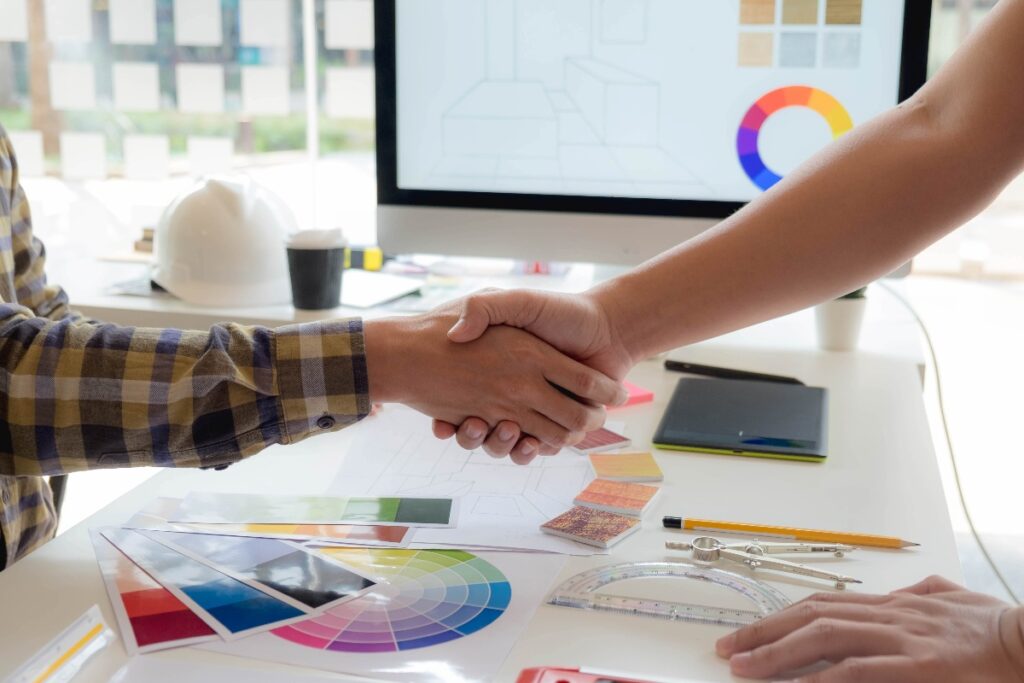 hands shaking in front of computer screen showing design elements