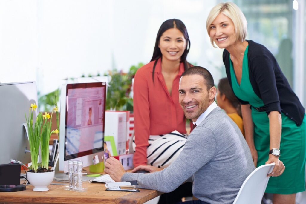 team working together and smiling in front of desk with computer
