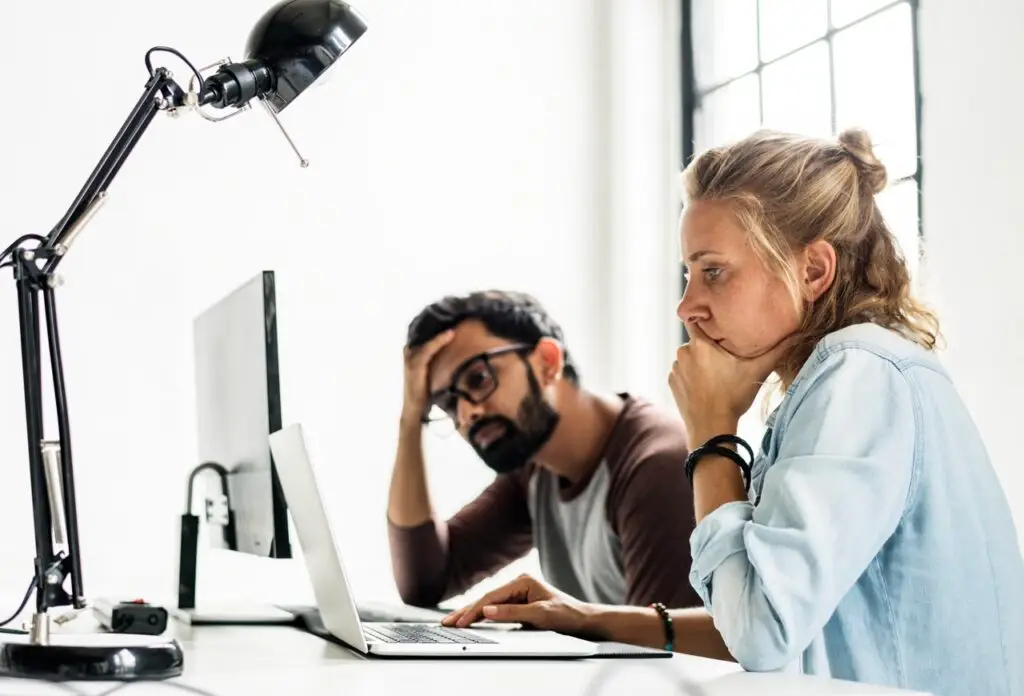 A male and a female each sitting in front of a computer screen frustrated and trying to figure out a fix