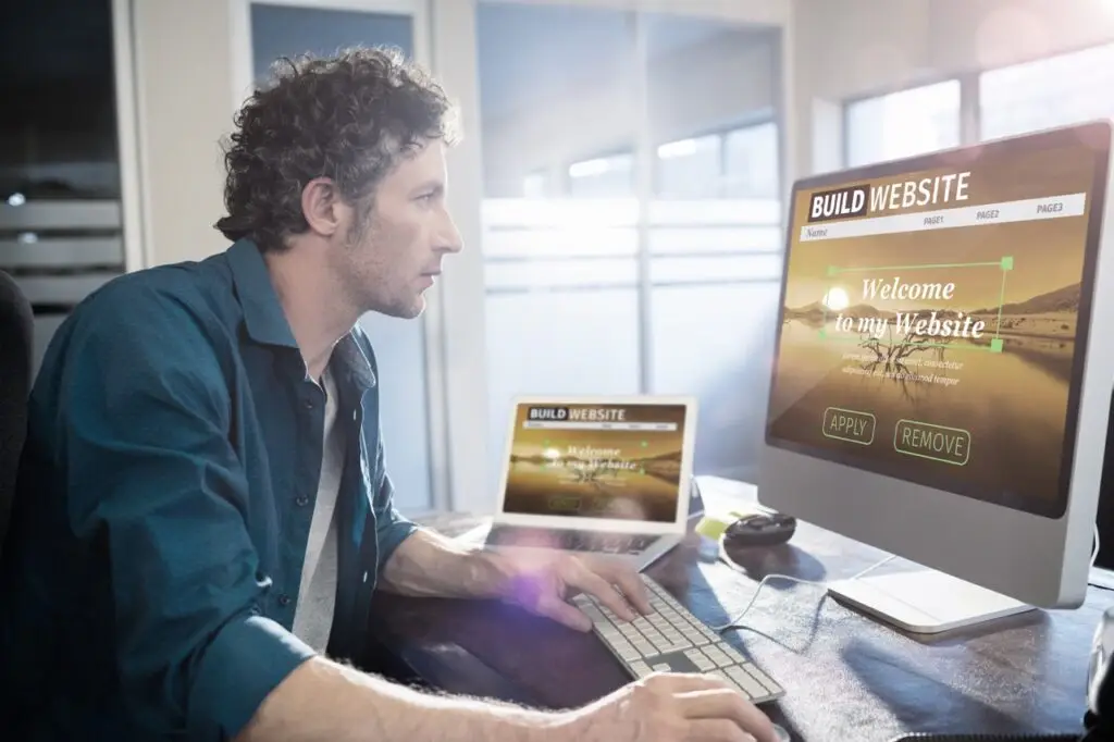 man in front of computer screen showing website being built